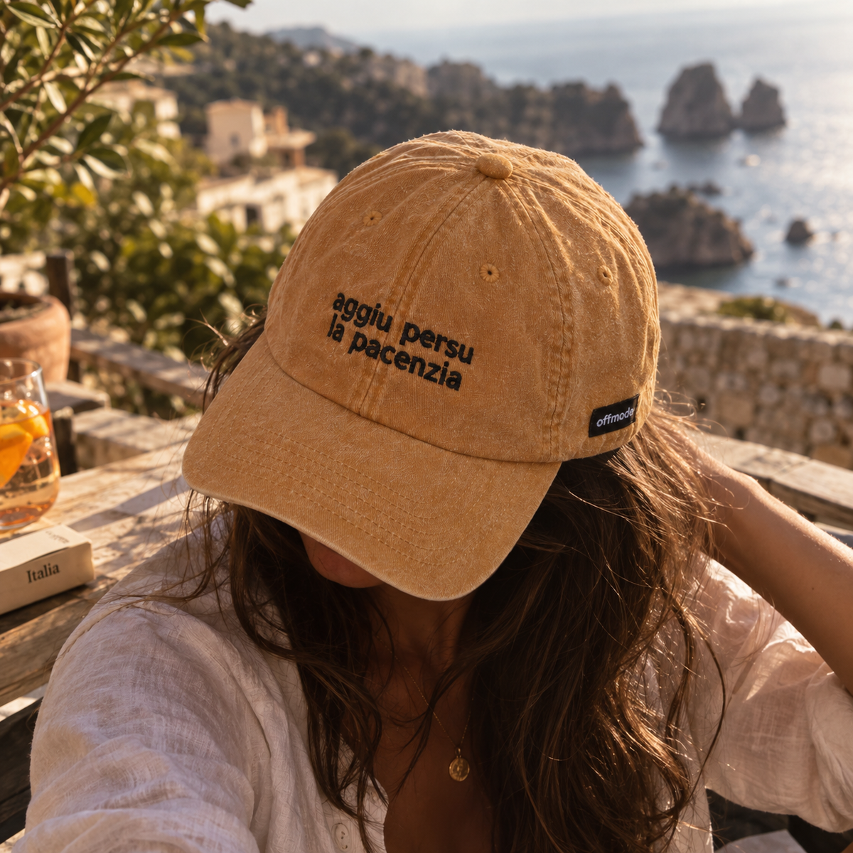 Cappello senape Offmode con la frase "aggiu persu la pacenzia" ricamata, indossato da una ragazza con la testa chinata