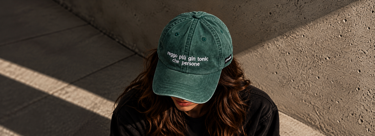 Cappello verde Offmode con la frase "reggo più gin tonic che persone" ricamata indossato da una donna con il volto chinato