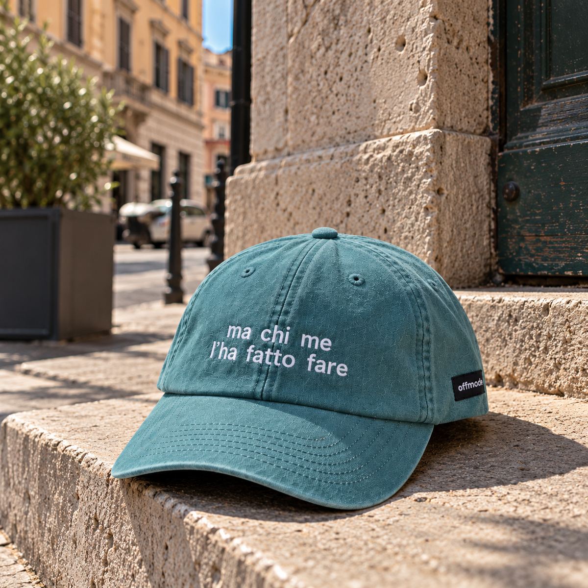 Cappello salvia Offmode con la frase "ma che me l'ha fatta fare" ricamata, poggiato su uno scalino