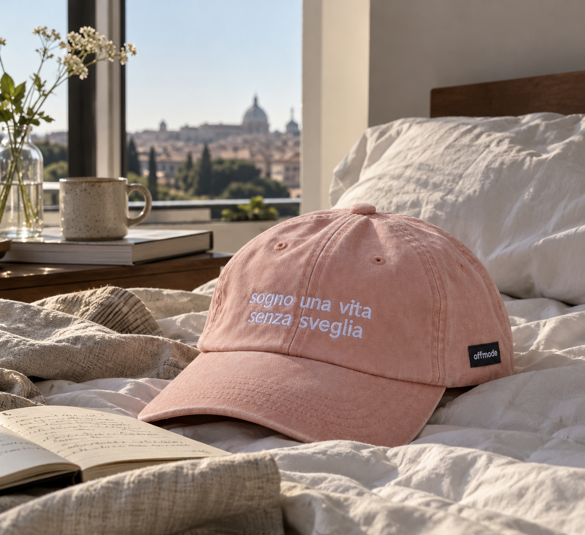 Un cappello sul letto color pesca Offmode con la frase "sogno una vita senza sveglia" ricamata